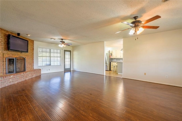 unfurnished living room with ceiling fan, a fireplace, dark wood-type flooring, and a textured ceiling