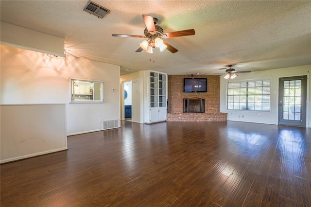 unfurnished living room featuring ceiling fan, a fireplace, dark wood-type flooring, and a textured ceiling