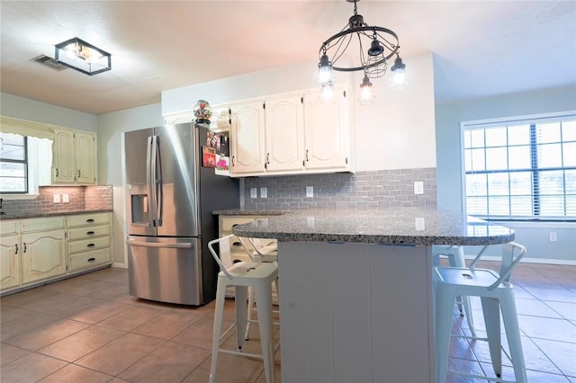 kitchen with a breakfast bar area, kitchen peninsula, stainless steel fridge, and a healthy amount of sunlight