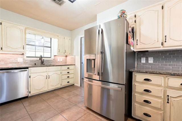 kitchen with sink, stainless steel appliances, dark stone counters, decorative backsplash, and light tile patterned floors