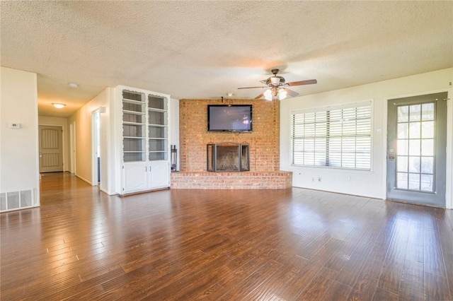 unfurnished living room with dark hardwood / wood-style flooring, a textured ceiling, and a brick fireplace