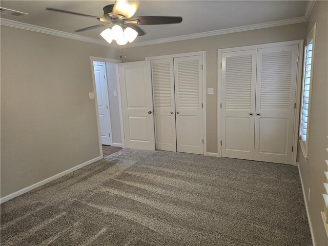 unfurnished bedroom featuring dark colored carpet, ceiling fan, ornamental molding, and two closets