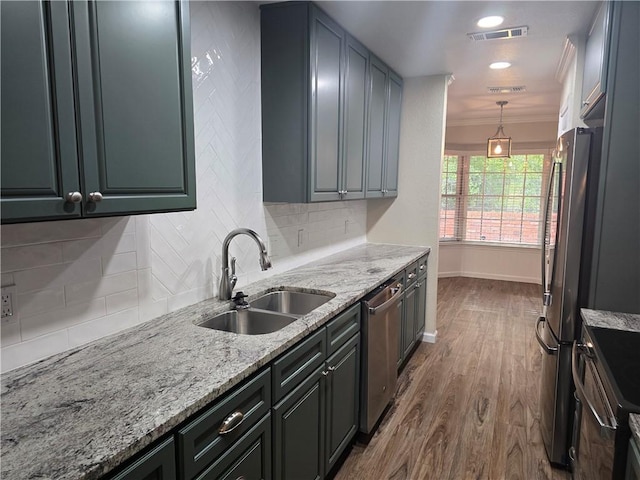 kitchen featuring light stone countertops, sink, hardwood / wood-style floors, pendant lighting, and appliances with stainless steel finishes