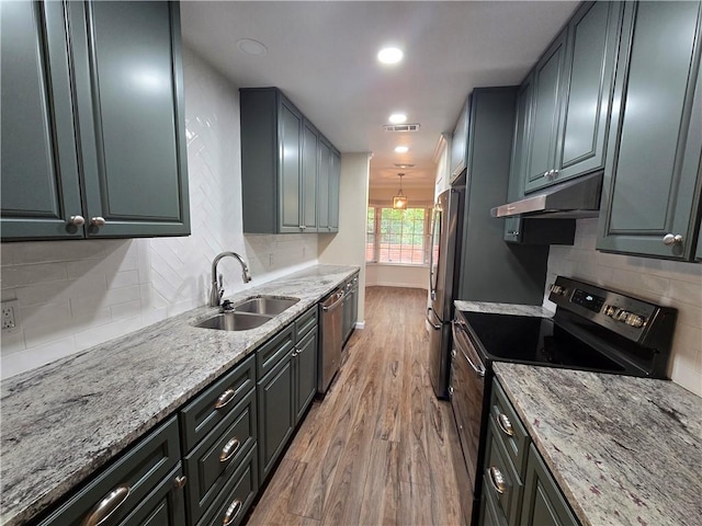 kitchen with tasteful backsplash, light stone counters, stainless steel appliances, sink, and light hardwood / wood-style floors