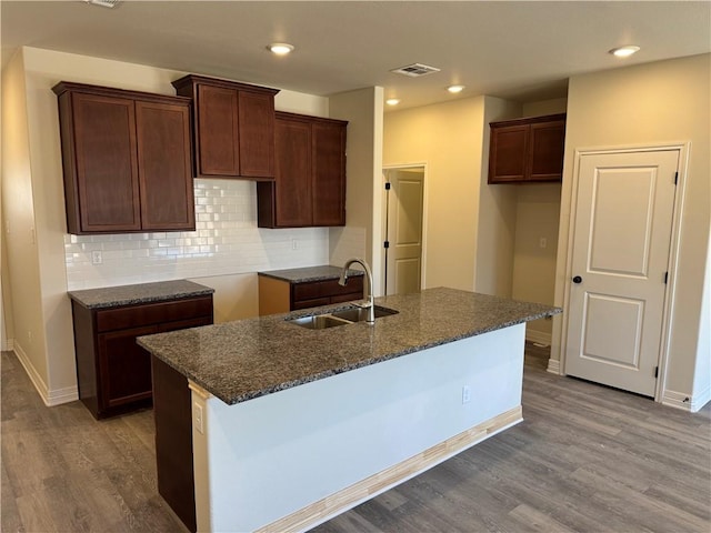 kitchen with decorative backsplash, an island with sink, light wood-style flooring, a sink, and recessed lighting