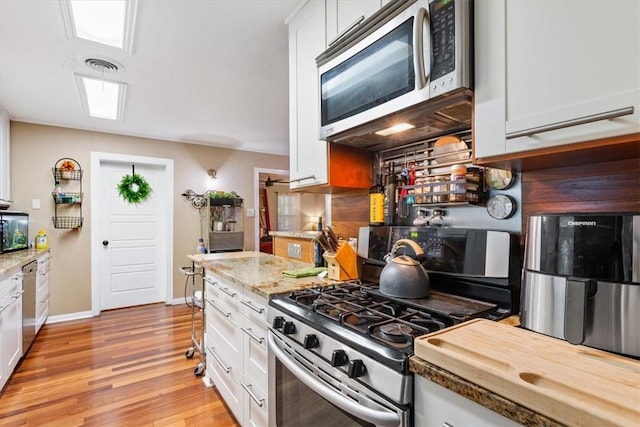 kitchen featuring light stone countertops, light wood-type flooring, appliances with stainless steel finishes, tasteful backsplash, and white cabinetry