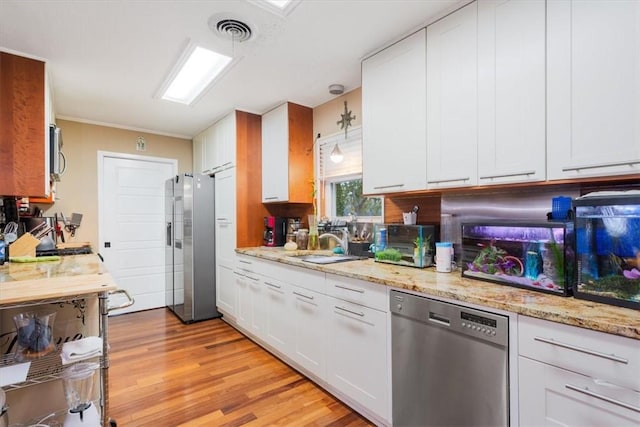 kitchen featuring appliances with stainless steel finishes, light wood-type flooring, sink, pendant lighting, and white cabinetry