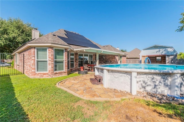 rear view of property with a lawn, solar panels, a storage shed, a fenced in pool, and a patio area