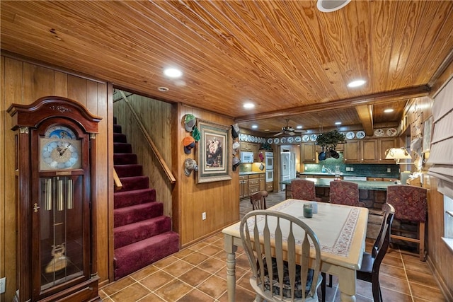 dining room featuring wooden walls, beamed ceiling, light tile patterned floors, and ceiling fan