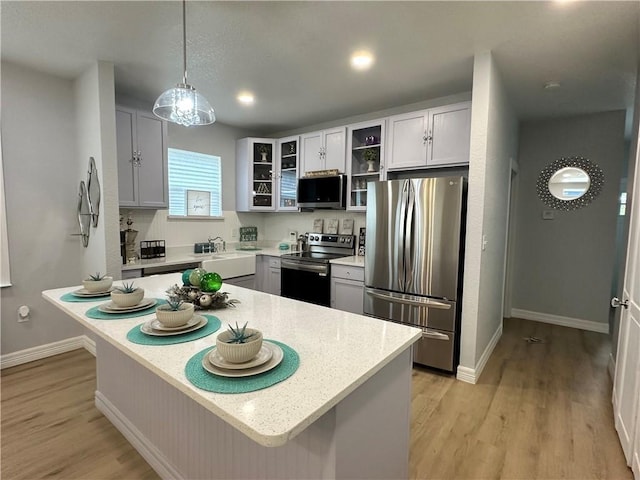 kitchen with hanging light fixtures, light wood-style flooring, appliances with stainless steel finishes, and glass insert cabinets