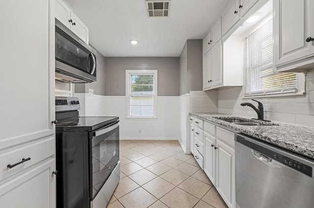 kitchen featuring white cabinets, sink, light stone countertops, light tile patterned floors, and stainless steel appliances