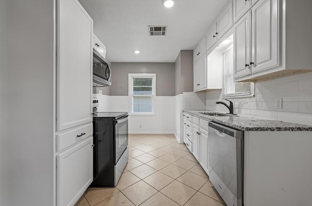 kitchen with sink, appliances with stainless steel finishes, stone countertops, light tile patterned flooring, and white cabinetry