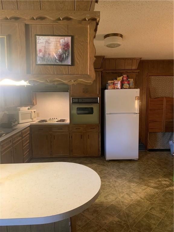 kitchen featuring a textured ceiling, wood walls, and white appliances