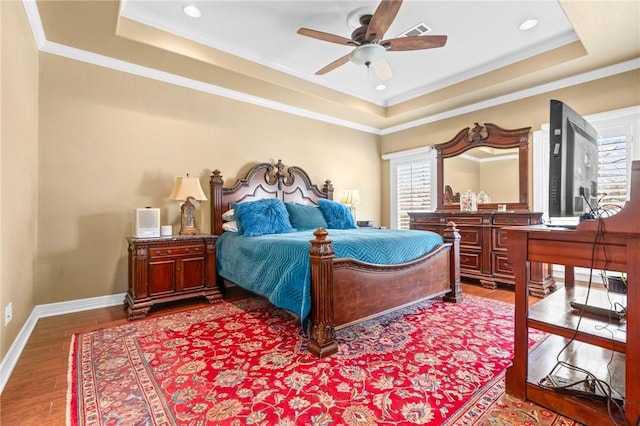 bedroom featuring a tray ceiling, baseboards, visible vents, and wood finished floors