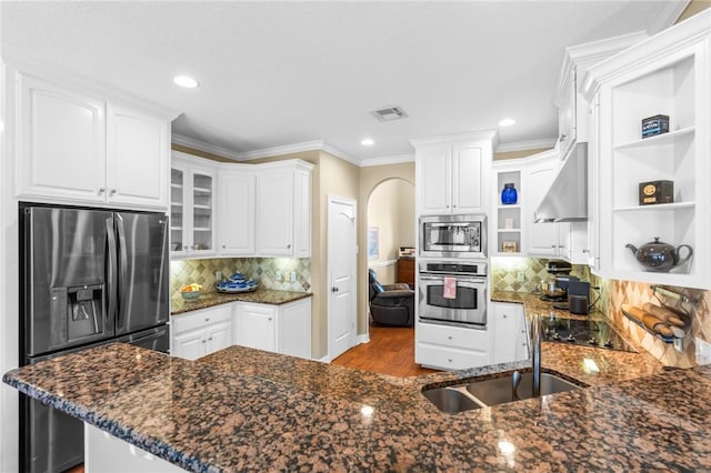 kitchen featuring open shelves, range hood, arched walkways, stainless steel appliances, and a sink