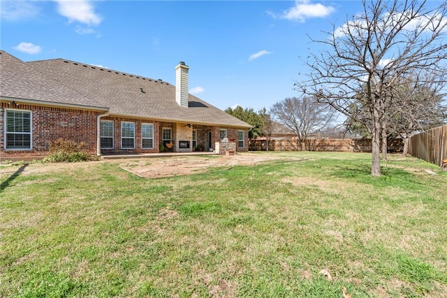 back of property featuring a patio, a fenced backyard, a yard, brick siding, and a chimney