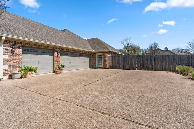 view of property exterior with fence, roof with shingles, concrete driveway, a garage, and brick siding