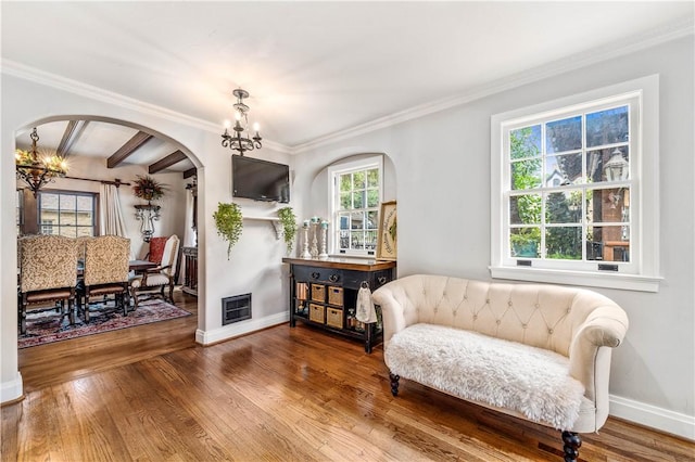 living area with hardwood / wood-style floors, ornamental molding, a notable chandelier, and beam ceiling