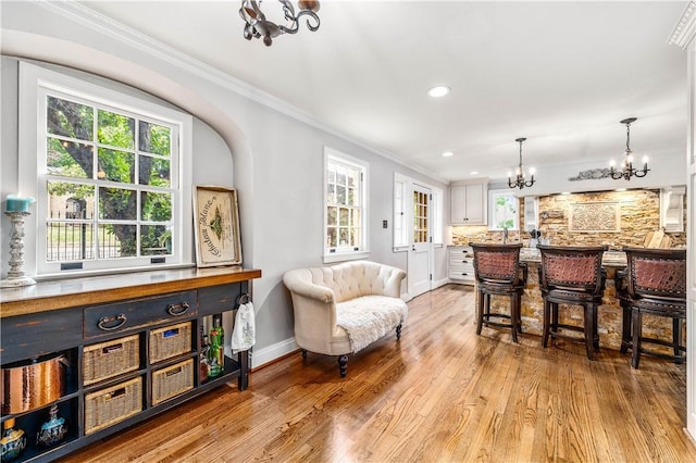 bar with white cabinetry, ornamental molding, a chandelier, and light wood-type flooring