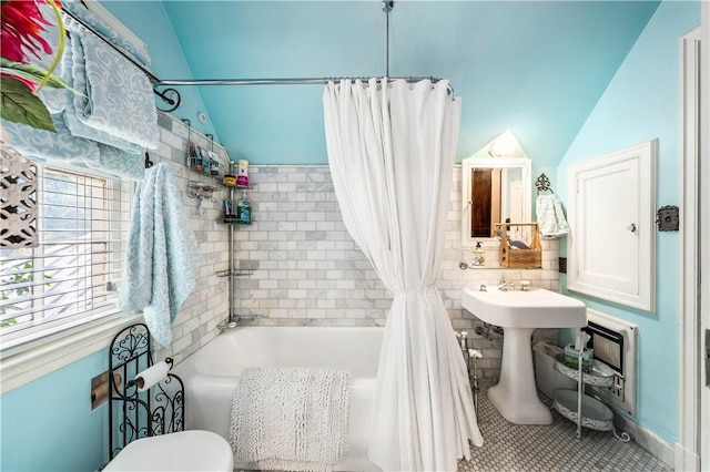 bathroom featuring lofted ceiling, tile patterned floors, toilet, tile walls, and shower / tub combo