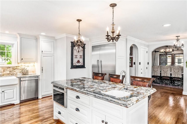 kitchen featuring light stone countertops, light hardwood / wood-style flooring, a center island with sink, white cabinets, and appliances with stainless steel finishes