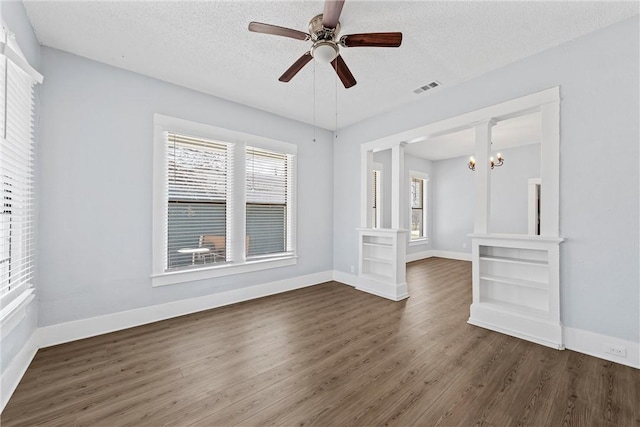 unfurnished room featuring a wealth of natural light, a textured ceiling, visible vents, and dark wood-type flooring