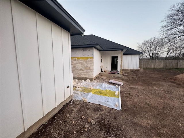 view of side of property featuring stone siding, board and batten siding, a shingled roof, and fence