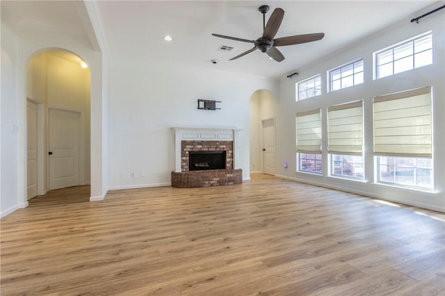 unfurnished living room with a high ceiling, ceiling fan, light wood-type flooring, and a fireplace