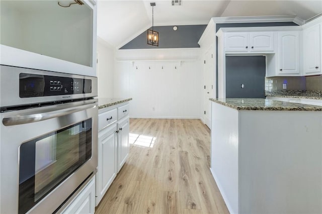 kitchen featuring white cabinetry, lofted ceiling, dark stone counters, hanging light fixtures, and stainless steel oven