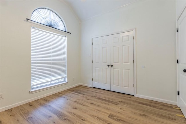 unfurnished bedroom with multiple windows, vaulted ceiling, and light wood-type flooring