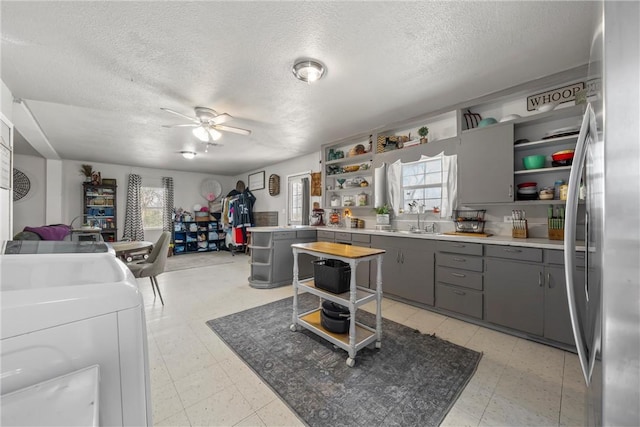 kitchen with washing machine and clothes dryer, sink, stainless steel refrigerator, gray cabinets, and ceiling fan