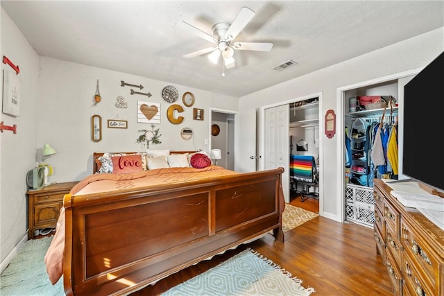 bedroom featuring ceiling fan, dark wood-type flooring, and multiple closets