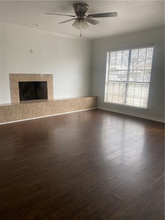 unfurnished living room featuring ceiling fan, a textured ceiling, dark wood-type flooring, and a tile fireplace