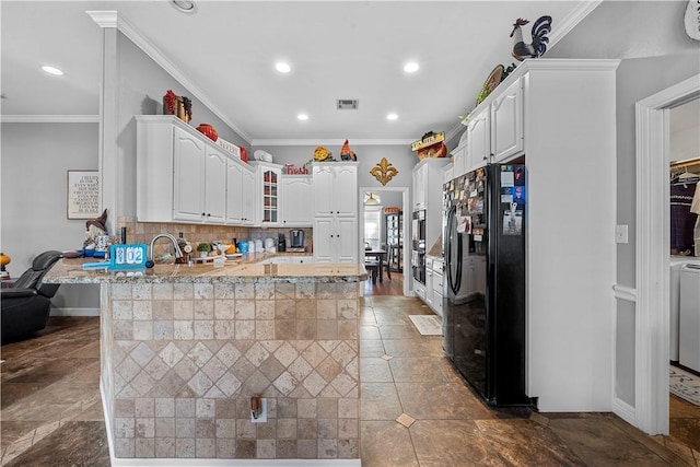 kitchen with black refrigerator, kitchen peninsula, light stone countertops, crown molding, and white cabinets