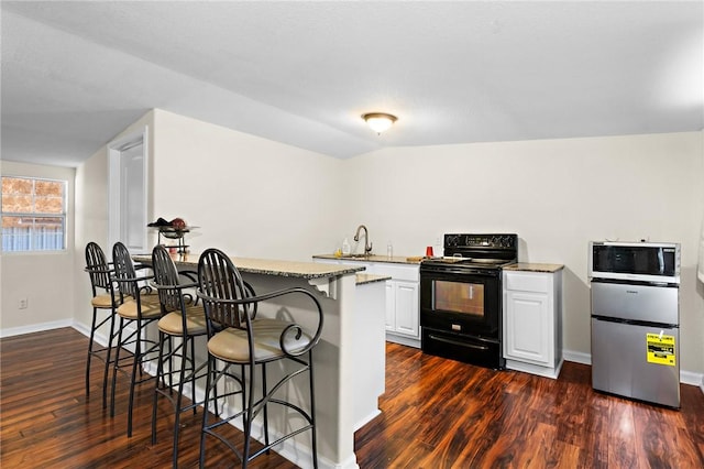 kitchen with a kitchen bar, stainless steel appliances, white cabinetry, and dark hardwood / wood-style floors