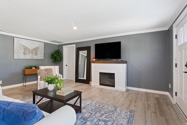 living area with ornamental molding, wood finished floors, a glass covered fireplace, and baseboards