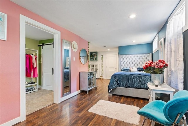 bedroom featuring a barn door, dark wood-style flooring, recessed lighting, and baseboards