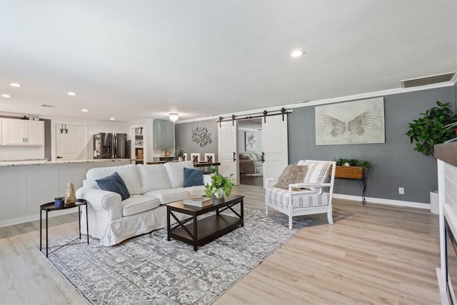 living area with a barn door, baseboards, ornamental molding, light wood-type flooring, and recessed lighting