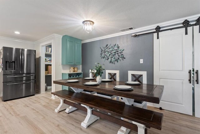 dining area featuring a barn door, light wood-type flooring, visible vents, and crown molding