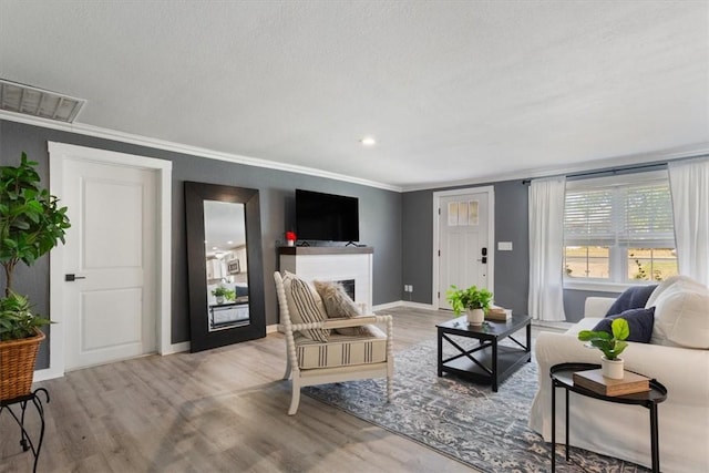 living room featuring crown molding, a fireplace, visible vents, wood finished floors, and baseboards