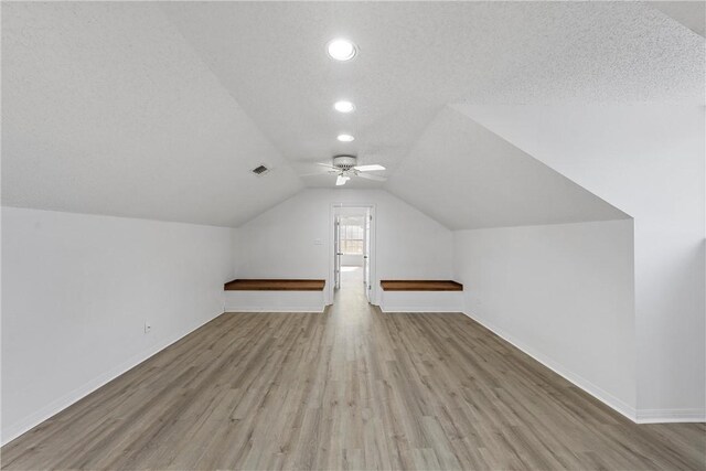 bonus room with a textured ceiling, vaulted ceiling, light hardwood / wood-style flooring, and ceiling fan