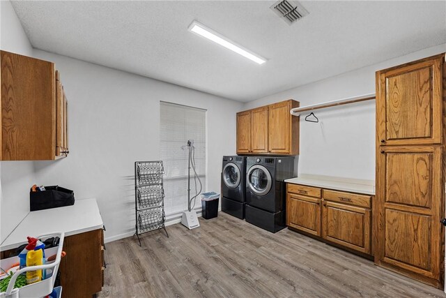 laundry room with cabinets, independent washer and dryer, a textured ceiling, and light hardwood / wood-style flooring