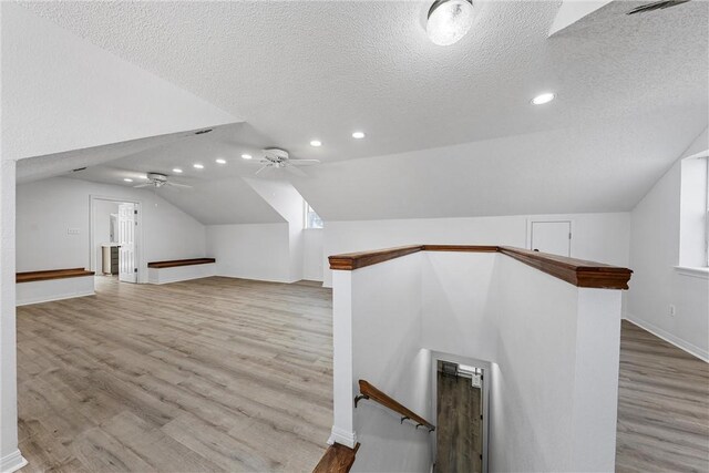 additional living space with a textured ceiling, light wood-type flooring, ceiling fan, and lofted ceiling