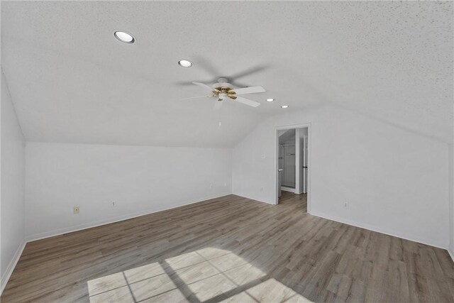 additional living space with ceiling fan, lofted ceiling, a textured ceiling, and light hardwood / wood-style flooring