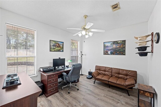 home office with a textured ceiling, light hardwood / wood-style flooring, a wealth of natural light, and ceiling fan