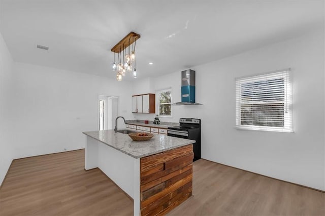 kitchen featuring sink, wall chimney range hood, pendant lighting, light hardwood / wood-style floors, and stainless steel electric stove