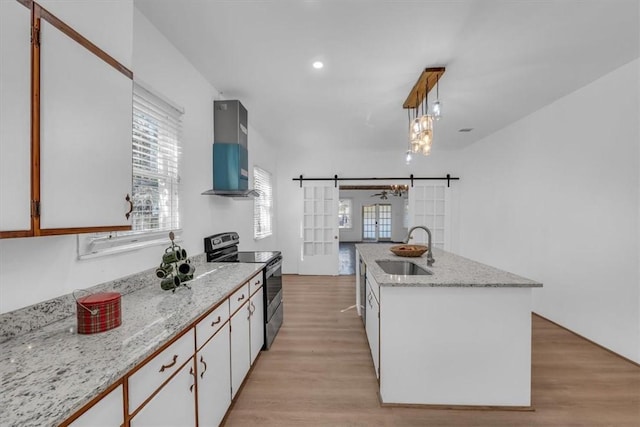 kitchen featuring a barn door, white cabinetry, a kitchen island with sink, and stainless steel electric range