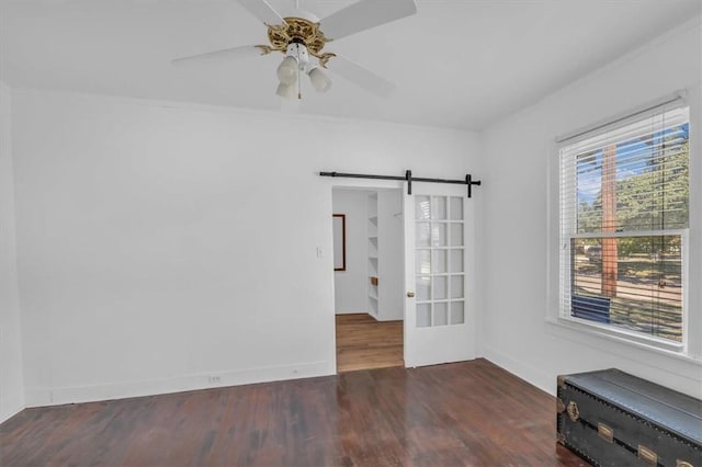 spare room with dark hardwood / wood-style flooring, a barn door, ornamental molding, and ceiling fan