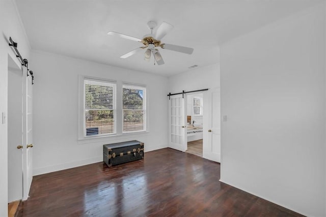 spare room with a barn door, dark hardwood / wood-style floors, and ceiling fan