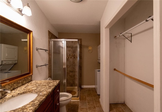 bathroom with vanity, toilet, a shower with shower door, and stacked washer and dryer